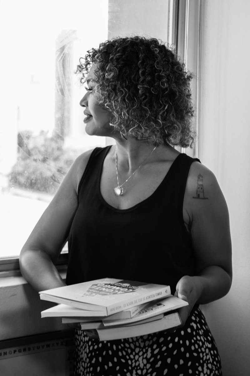 Débora Luiza de Souza junto à janela, segurando livros de psicologia